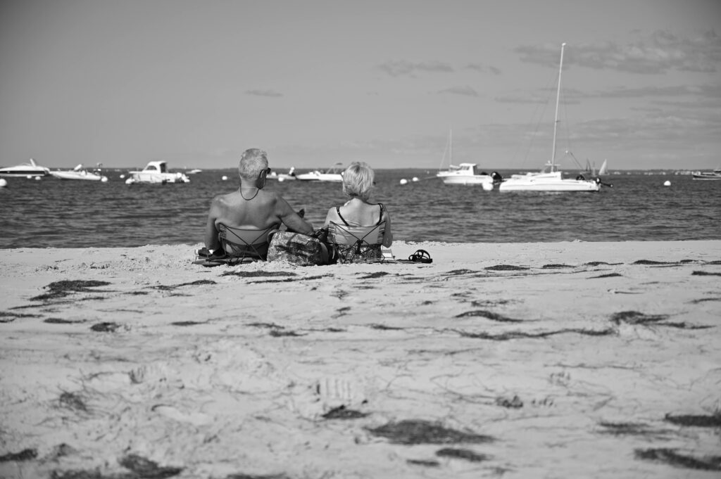 pexels-photo-29885731-29885731 Black and white photo of an elderly couple seated on a sandy beach in Arcachon, France, enjoying the sea view.